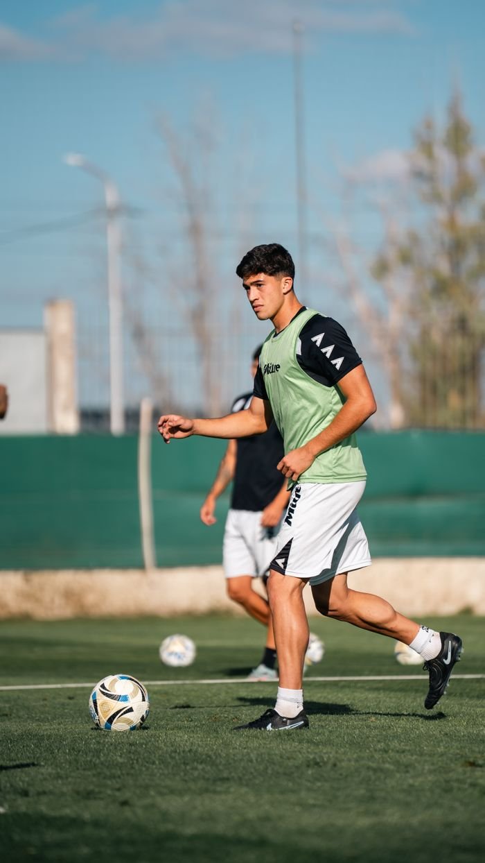 Teenage soccer player practicing on an outdoor field during the day with peers.